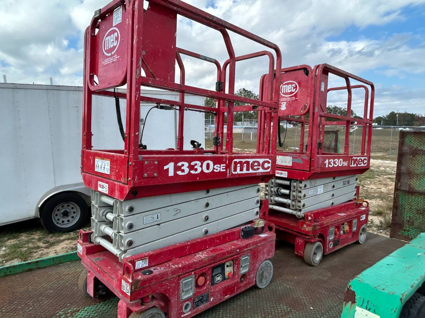 Two red MEC scissor lifts parked outdoors