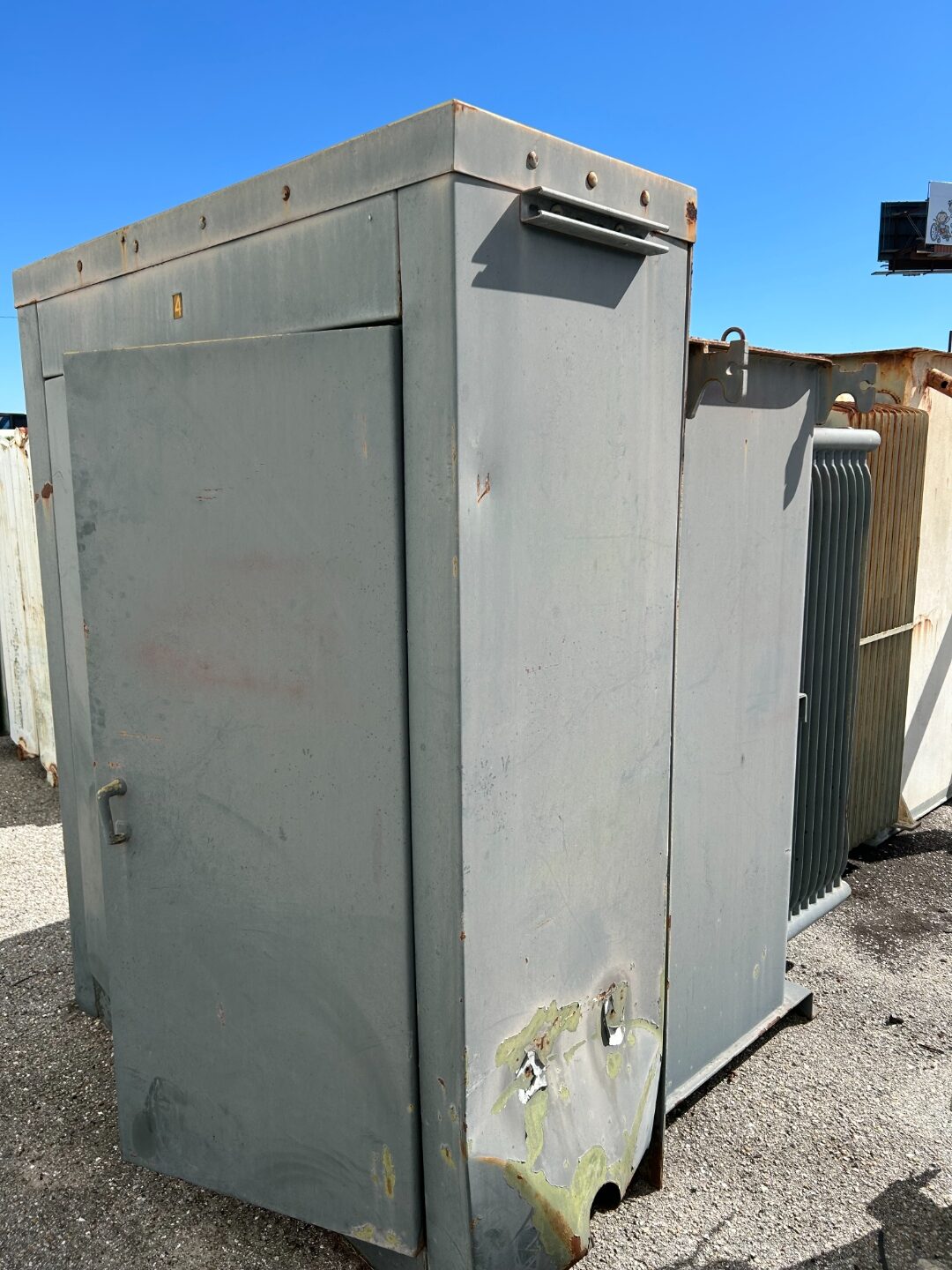 Large gray power transformer with radiator fins staged in a yard